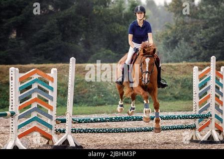 Junge Reiterin Mädchen springen über eine Barriere auf Springkurs im Reitsport Wettbewerb. Stockfoto