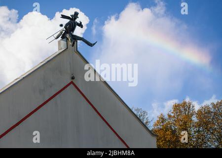Schornsteinfeger Skulptur auf dem Dach in der Altstadt von Klaipeda, Litauen. Hausmauer in der Altstadt von Klaipeda. Blauer Himmel mit weißen Wolken und Regenbogen. Stockfoto