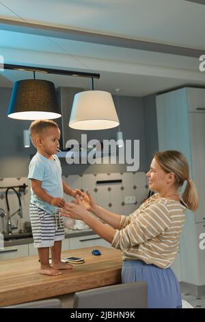 Porträt von glücklichen kaukasischen Mutter spielt mit niedlichen Kleinkind Junge in der Küche zu Hause Innenraum Stockfoto