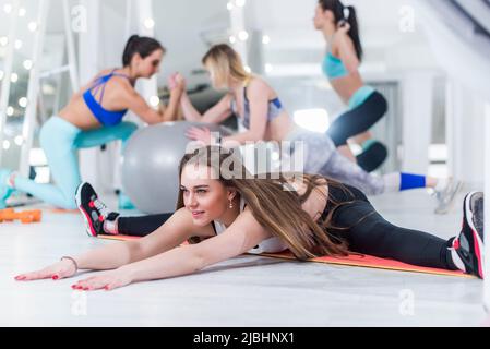 Fit junge Frauen trainieren in der Turnhalle mit lächelnden jungen Mädchen im Fokus tun vollständige Spaltung nach vorne lehnen. Stockfoto