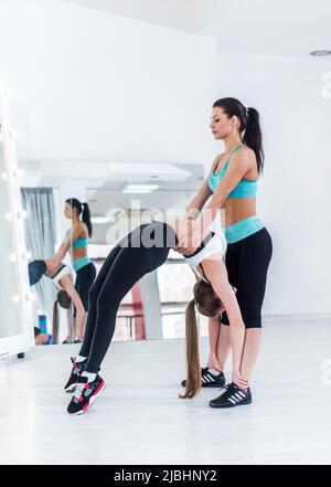 Die junge kaukasische Frau, die mit Hilfe eines persönlichen Trainers eine fortgeschrittene Krabbenposition einnimmt und ihren Rücken im Fitnessstudio unterstützt. Stockfoto