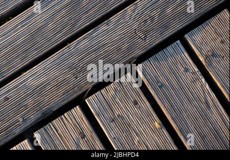 Ein Spiel von Lichtern und Schatten auf den Brettern eines hölzernen Piers. Das Licht, das in einem hohen Winkel auf die Bretter fällt, betont die Struktur des Materials Stockfoto