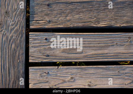 Ein Spiel von Lichtern und Schatten auf den Brettern eines hölzernen Piers. Das Licht, das in einem hohen Winkel auf die Bretter fällt, betont die Struktur des Materials Stockfoto