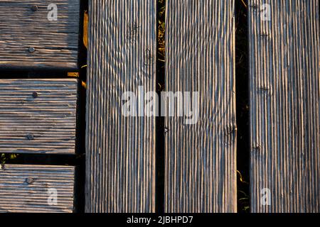 Ein Spiel von Lichtern und Schatten auf den Brettern eines hölzernen Piers. Das Licht, das in einem hohen Winkel auf die Bretter fällt, betont die Struktur des Materials Stockfoto