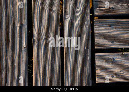 Ein Spiel von Lichtern und Schatten auf den Brettern eines hölzernen Piers. Das Licht, das in einem hohen Winkel auf die Bretter fällt, betont die Struktur des Materials Stockfoto