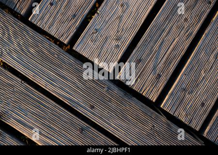 Ein Spiel von Lichtern und Schatten auf den Brettern eines hölzernen Piers. Das Licht, das in einem hohen Winkel auf die Bretter fällt, betont die Struktur des Materials Stockfoto