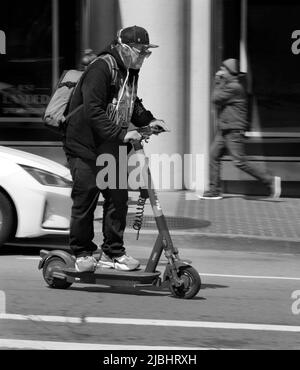 Ein Mann reist mit einem batteriebetriebenen Elektroroller auf einer belebten Straße in San Francisco, Kalifornien, entlang. Stockfoto