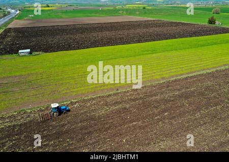 Luftaufnahme des Landwirts Traktor Pflügen auf dem Feld, Traktor Vorbereitung Land Saatbett Grubber im Frühjahr Stockfoto