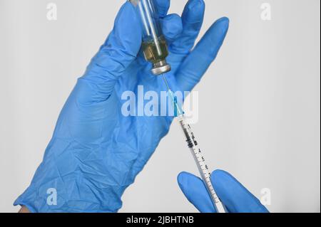 Die Hände des Arztes in blauen Handschuhen halten eine Spritze und einen Impfstoff. Das Konzept der Immunisierung. Stockfoto