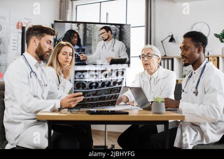 Gruppe multiethnischer medizinischer Forscher, die ein entferntes Video-Webinar mit professionellen Kollegen im Konferenzsaal des Labors abhalten. Wissenschaftler sprechen darüber Stockfoto