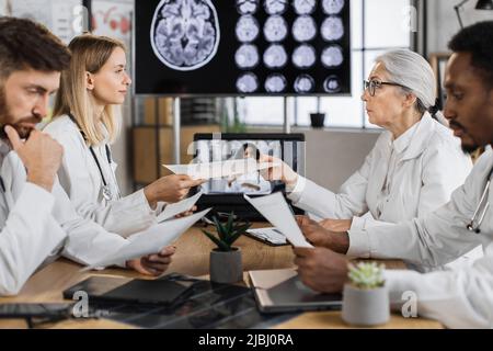 Konzentrieren Sie sich auf zwei verschiedene Altersgruppen Wissenschaftlerinnen teilen Präsentationsliste während des Treffens im modernen Labor. Erfahrene multikulturelle Forscher mak Stockfoto