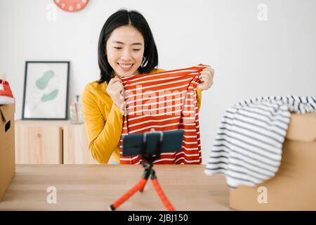 Junge asiatische Frau vlogging über Nachrichten Trends Kleidung Produkt mit Handy Stockfoto