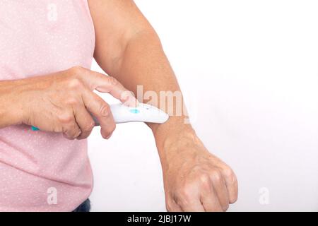 Eine Frau behandelt einen Mückenstich auf ihrem Arm mit einer elektrischen Bissheilerin - isoliert auf weißem Hintergrund. Stockfoto