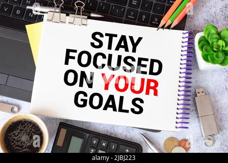 Inspirierendes Zitat – Bleib auf deine Ziele konzentriert. Mit Textnachricht auf weißem Papier Buch, Stift, eine Tasse Kaffee am Morgen, Blume. Stockfoto