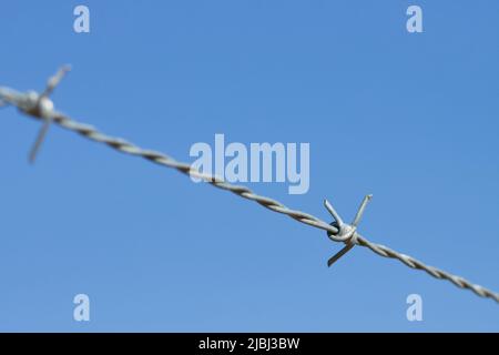 Bild des Stacheldrahtes, der einen Sicherheitszaun bildet, um Diebstahl auf Privateigentum zu verhindern, im Hintergrund der blaue Himmel Stockfoto