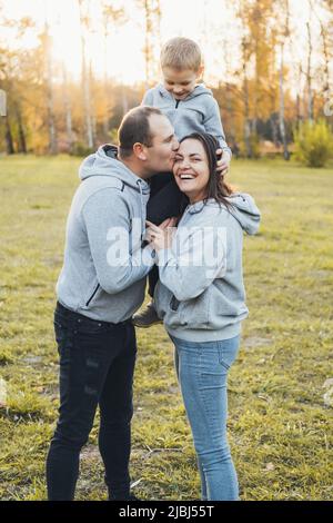 Eltern, die ihren Sohn auf den Schultern tragen, während sie im Park posieren. Aktivitätsbeziehung. Froher Sommer. Stockfoto