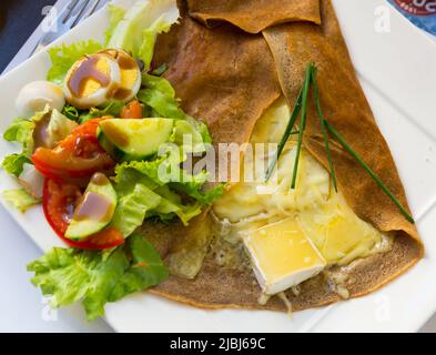 Gebratener Pfannkuchen mit geschmolzenem Käse und Salat, Gericht der französischen Küche Stockfoto
