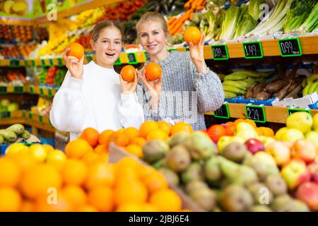 Glückliches Teenager-Mädchen mit Mutter hält reifen Orangen in greengrocery speichern Stockfoto