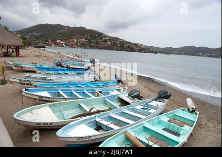 Panoramablick auf Fischerboote am Strand mit Palmen und Hügeln in Zihuatanejo, Mexiko Stockfoto