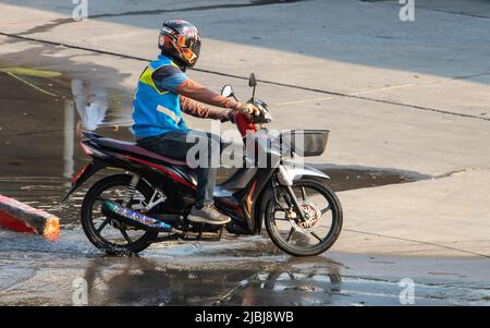 Der mototaxi-Fahrer in einer blauen Weste fährt auf der nassen Straße Stockfoto