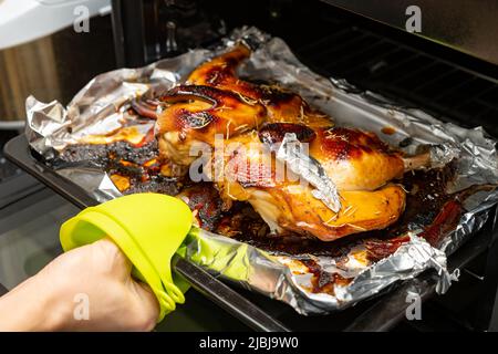 dame nimmt ein frisch gebackenes hausgemachtes Huhn aus dem Ofen Stockfoto