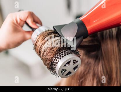 Der Friseur trocknet langes braunes Haar mit einem runden Pinsel. Hochwertige Fotos Stockfoto