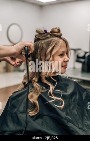 Niedliches Kind, das Haare gemacht hat. Friseur mit Lockenstab. Generation der Mode. Hochwertige Fotos Stockfoto