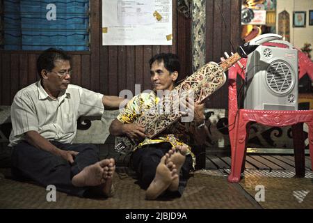 Ein Mann, der im Bali Gundi Longhouse der traditionellen Dayak Taman Gemeinde in Sibau Hulu, Putussibau Utara, Kapuas Hulu, West Kalimantan, Indonesien, ein traditionelles Saiteninstrument von Dayaknese spielt. Stockfoto