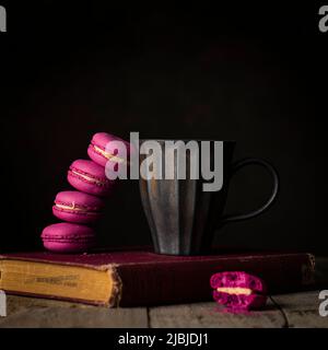Erdbeer-Macaron mit antiker Kaffeetasse oben auf altem Buch Stockfoto