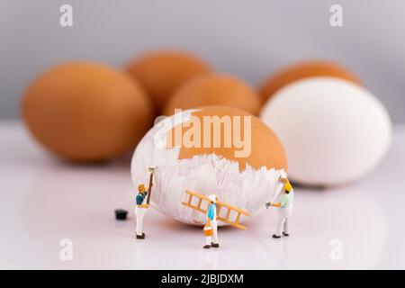 Miniatur Menschen kleine Modell menschliche Figur malen braune Eier zu weiß Stockfoto
