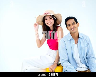 Paar Reisende bereit zu reisen, glücklicher Urlaub. Farbenfroher Sommerurlaub. Junge Schönheit asiatische Frau mit Strandhut, Mann in Denim-Hemd sitzt zusammen Stockfoto