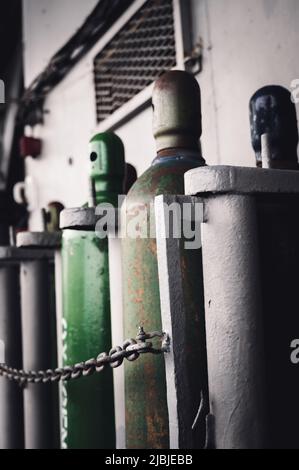 Druckgasflaschen, die vertikal durch eine Metallkette gesichert gelagert werden. Stockfoto