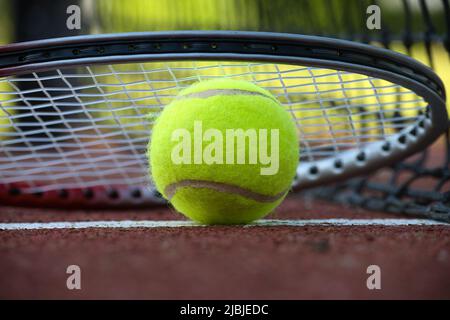 Nahaufnahme der Tennisrakete über dem gelben Tennisball auf Hartplätzen in der niedrigen Ansicht Stockfoto