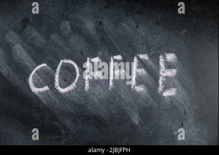 Das halbgelöschte Wort KAFFEE auf schwarzer Tafel. Handgeschriebenes Wort. Unscharfe Buchstaben auf schwarzer Oberfläche. Stockfoto