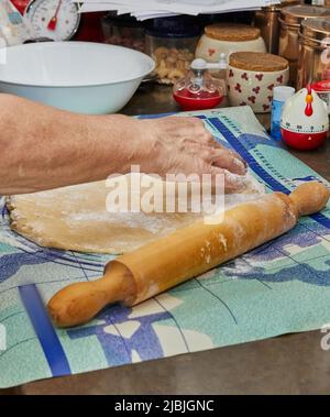 Frau rollt den Teig mit Nudelholz in der Küche aus, um Kuchen zu machen Stockfoto