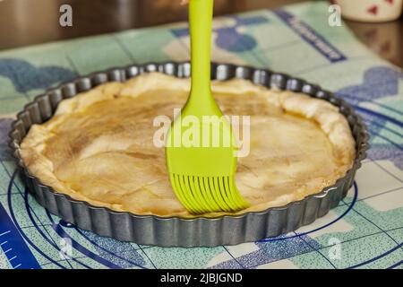 Der Koch verwendet eine spezielle Bürste, um den Pie-Teig vor dem Backen im Ofen mit dem Ei zu bürsten Stockfoto