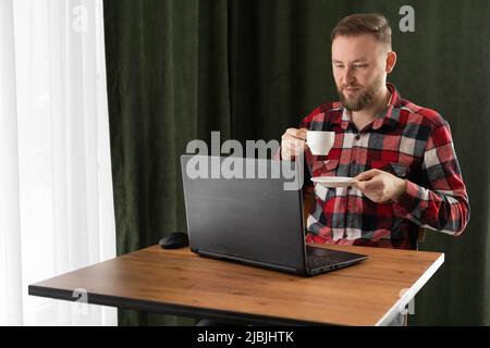 Ernst kaukasischer Geschäftsmann, der im Heimbüro am Laptop arbeitet. Junge europäische Schüler oder Fernlehrer mit Computer-Fernunterricht virtuell Stockfoto