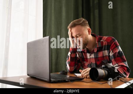 Frustrierter Fotograf beim Laden von Dateien auf den Laptop. Überprüfen von Fotos im modernen Büro. Bearbeitung seiner Bilder auf Laptop. Problem Stockfoto