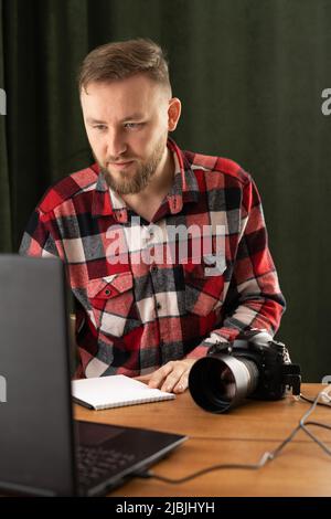 Professioneller Fotograf mit Kamera und Laptop im Studio. Fotograf mit Assistent, der im Büro sitzt und die Kamera anschaut Stockfoto