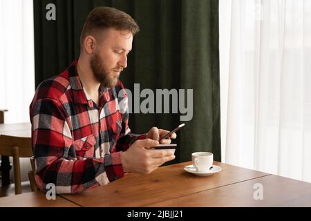 Glücklicher kaukasischer Mann, der das Mobiltelefon hält, um Kartendaten einzugeben, um Online-Zahlungen im Café oder beim Online-Shopping zu tätigen Stockfoto