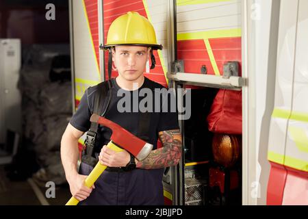 Foto von Feuerwehrmann mit Helm und Axt gegen Feuerwehrmann. Stockfoto