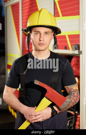 Foto von Feuerwehrmann mit Helm und Axt gegen Feuerwehrmann. Stockfoto