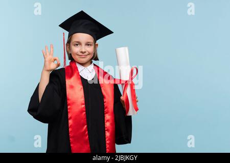 Whizz Kind 9-11 Jahre Mädchen trägt Abschlusskappe und Zeremonie Robe mit Zertifikat Diplom auf blauem Hintergrund. Kind Mädchen haben positive Emotionen, zeigen Stockfoto