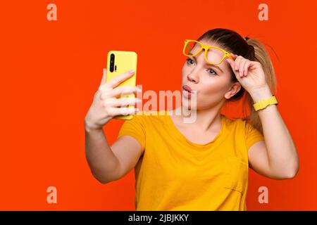 Schockiert überrascht Mädchen in legeren gelben tragen und Brillen sieht in Handy. Junge Frau macht lustige Gesicht. Konzept Emotionen, Gesichtsausdruck. Adva Stockfoto