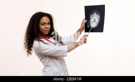 Dunkelhäutig Ärztin untersucht einen Röntgenscan auf hellem Hintergrund. Der Radiologielehrer schaut in die Kamera. Stockfoto