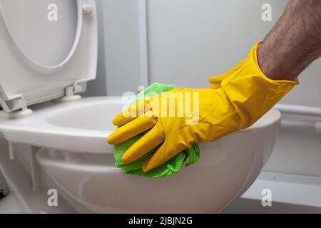 Der Mann reinigt eine Toilette im Badezimmer mit einer grünen Bürste Stockfoto