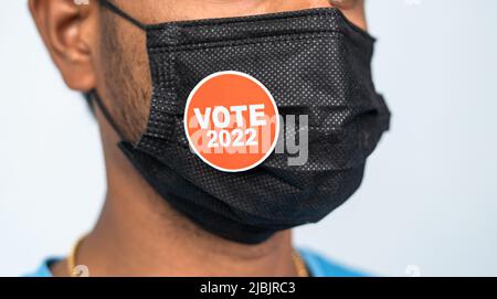 Fokus auf Maske, Nahaufnahme einer jungen Mna mit Sticker Votum 2022 auf medizinischer Gesichtsmaske - Konzept der Wahlen 2022 während des Coronavirus oder Covid-19 Stockfoto