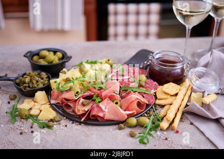 Zwei Gläser Weißwein und italienische Antipasto-Fleischplatte in der heimischen Küche Stockfoto