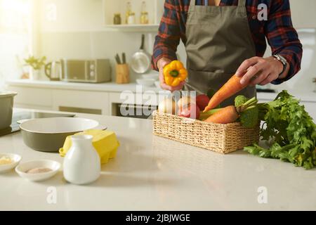 Beschnittenes Bild des Mannes, der frisches, reifes Gemüse für das Gericht wählt, das er gerade kocht Stockfoto