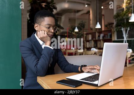 Junge Geschäftsfrau, die arbeitet, ist ein Café mit einem Laptop, afroamerikanisch konzentriert sich auf das Ende des Projekts, die Frist ist für die Mittagspause Stockfoto